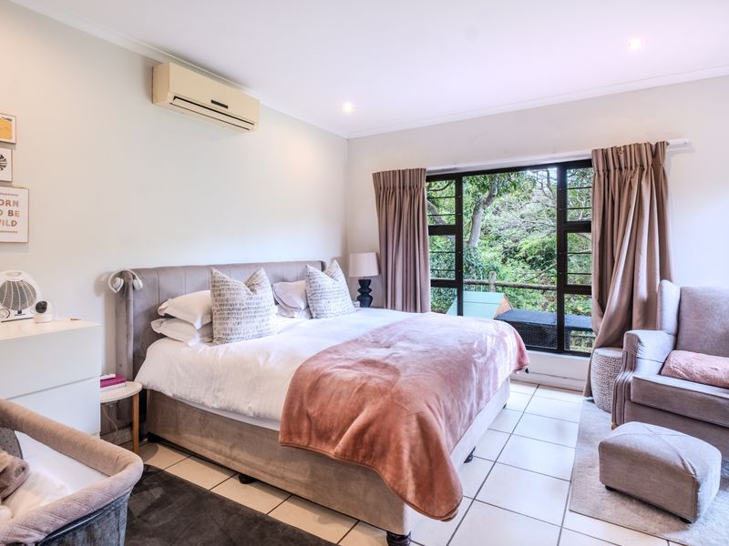 A well-lit bedroom featuring tiled flooring, a wall-mounted air conditioning unit, and a large window overlooking lush greenery.