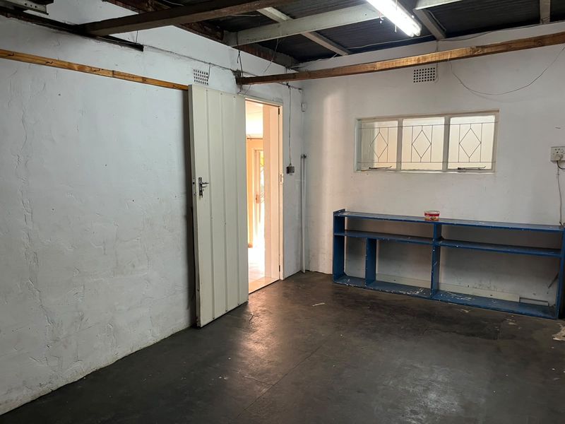 A functional garage space featuring exposed ceiling beams, concrete flooring, and built-in shelving, offering potential for storage or workshop use.