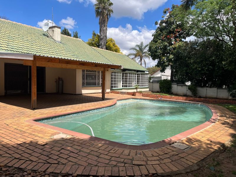 Outdoor entertainment area featuring a swimming pool, covered brick-paved patio, and established garden surroundings.