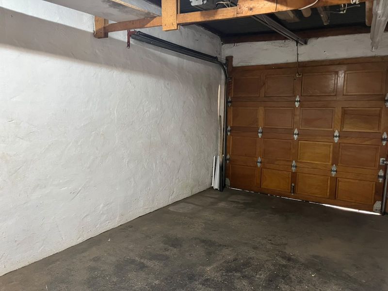 A functional garage space featuring a wooden sectional door, exposed timber ceiling beams, and a concrete floor.