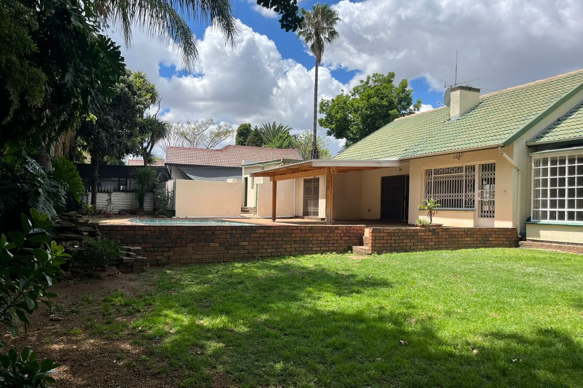 Rear view of the property featuring a swimming pool, a raised brick patio area with a timber-covered pergola, and a well-maintained garden.