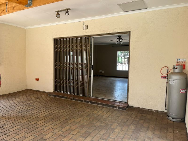 Covered patio area featuring brick paving, exposed timber beams, and a sliding security gate providing access to the interior living space.