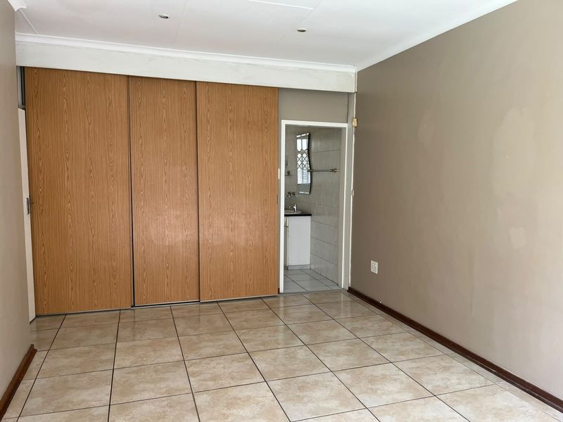 A vacant bedroom featuring tiled flooring, built-in sliding door cupboards, and direct access to an en-suite bathroom.