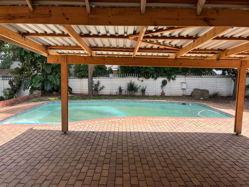 Outdoor entertainment area featuring a covered timber pergola, brick-paved patio, and a swimming pool set against a secure boundary wall.