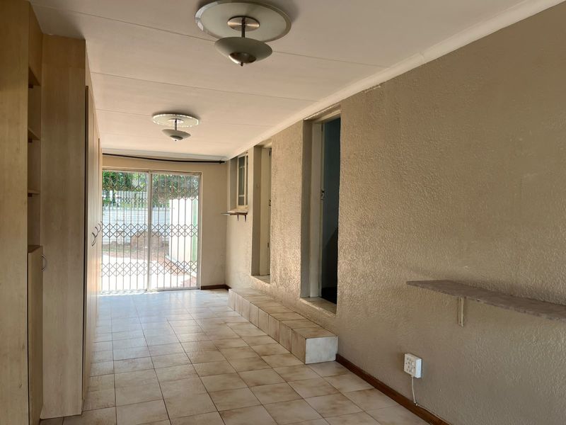 An empty living area featuring tiled flooring, built-in cupboards, and a sliding door with a security gate leading to the exterior.