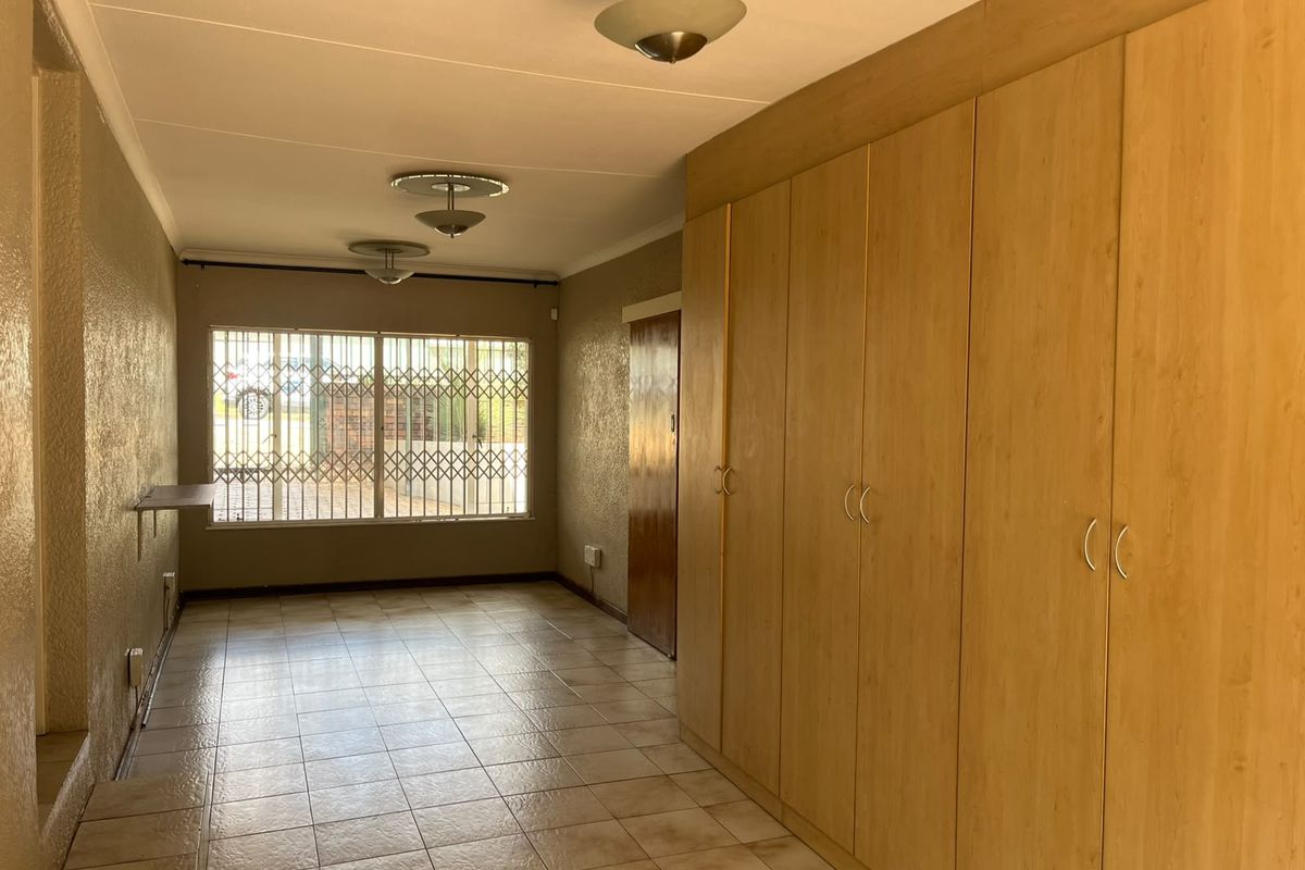 Spacious bedroom featuring extensive built-in wooden cupboards, tiled flooring, and a large window with security bars for added peace of mind.