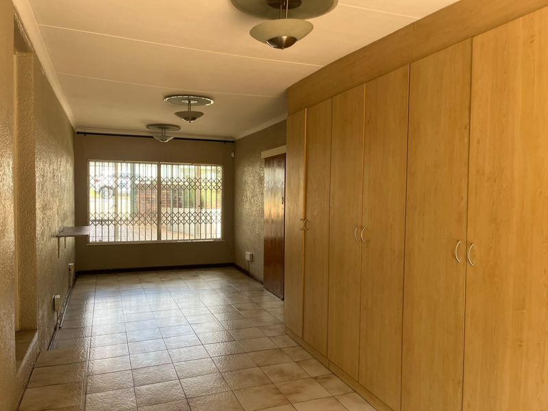 Spacious bedroom featuring extensive built-in wooden cupboards, tiled flooring, and a large window with security bars for added peace of mind.
