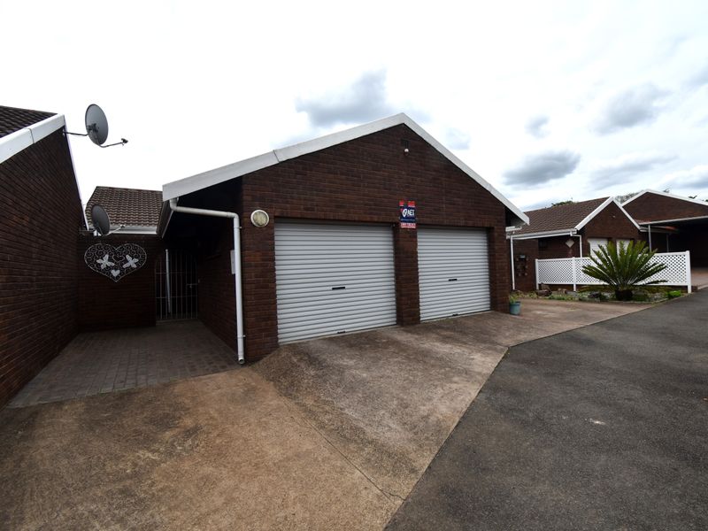 A double garage with roller doors and a paved driveway, featuring a classic brick exterior finish.