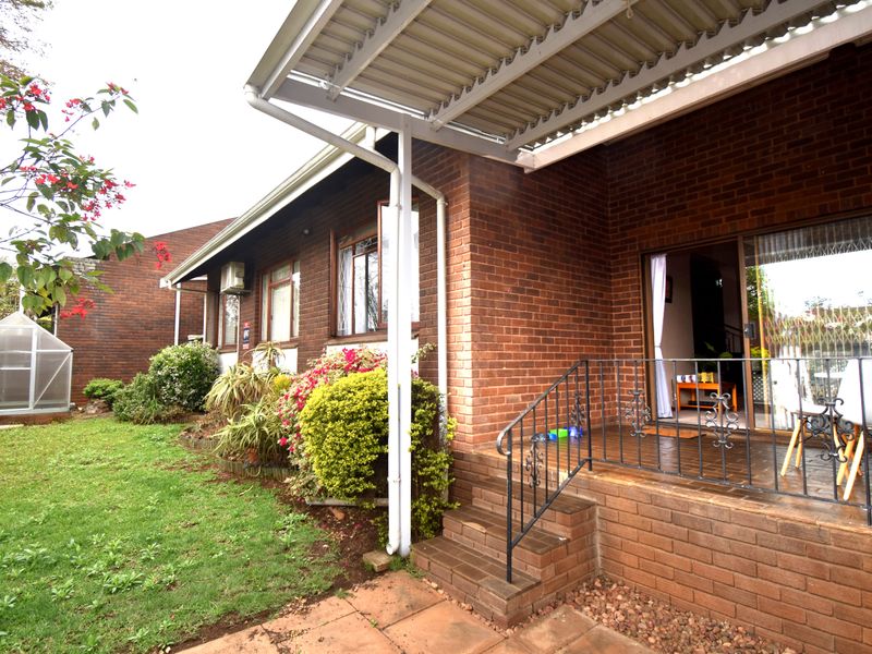 A covered brick patio area featuring wrought iron railings and sliding door access to the interior, overlooking a private garden space.