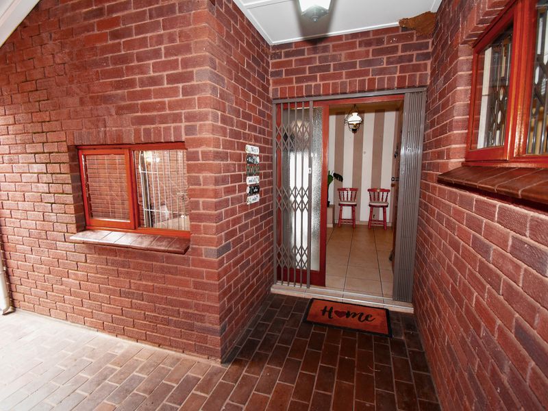 A covered brick entrance area featuring a security gate and tiled flooring, providing access to the interior of the townhouse.