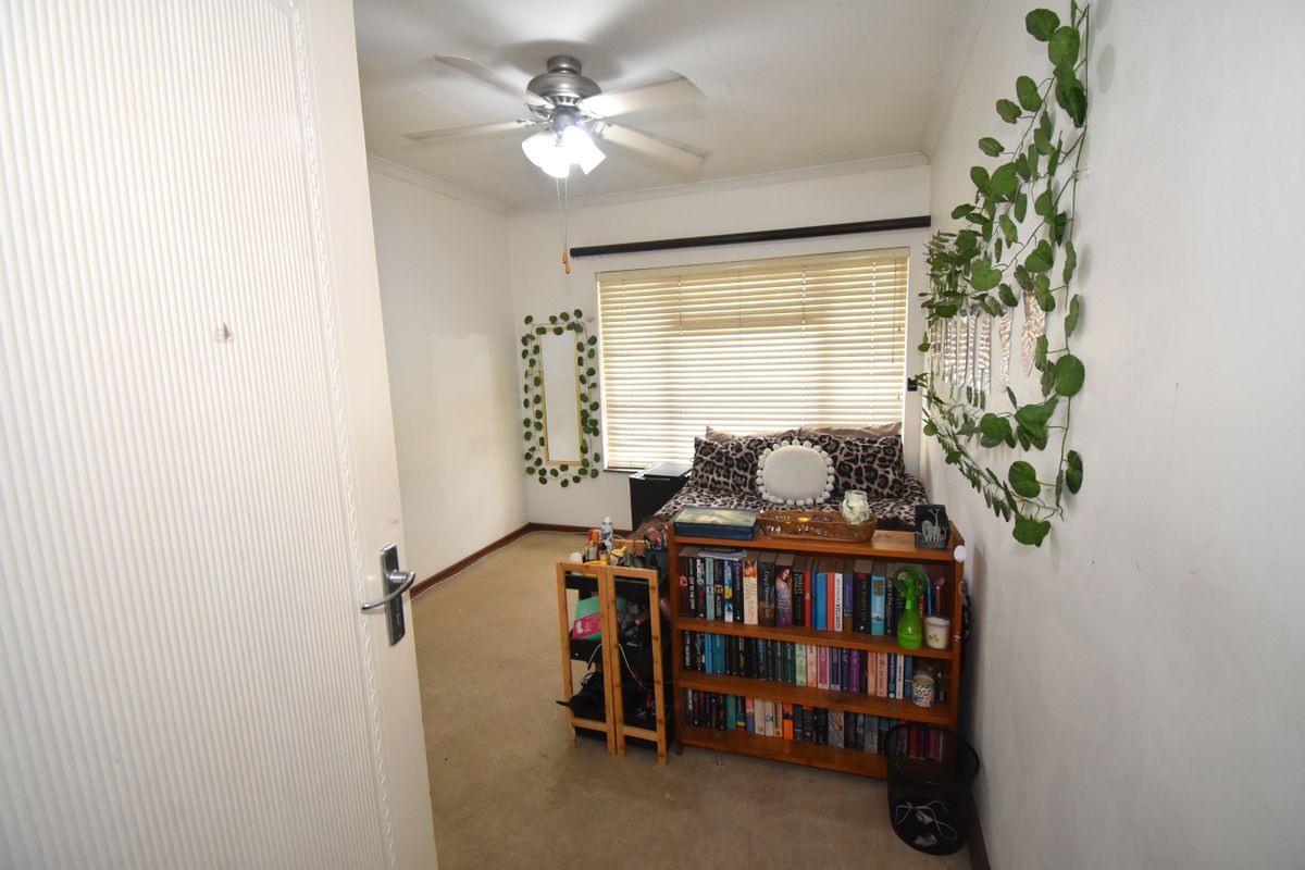 A standard bedroom featuring carpet flooring, a ceiling fan, and venetian blinds, offering a functional space ready for personalization.