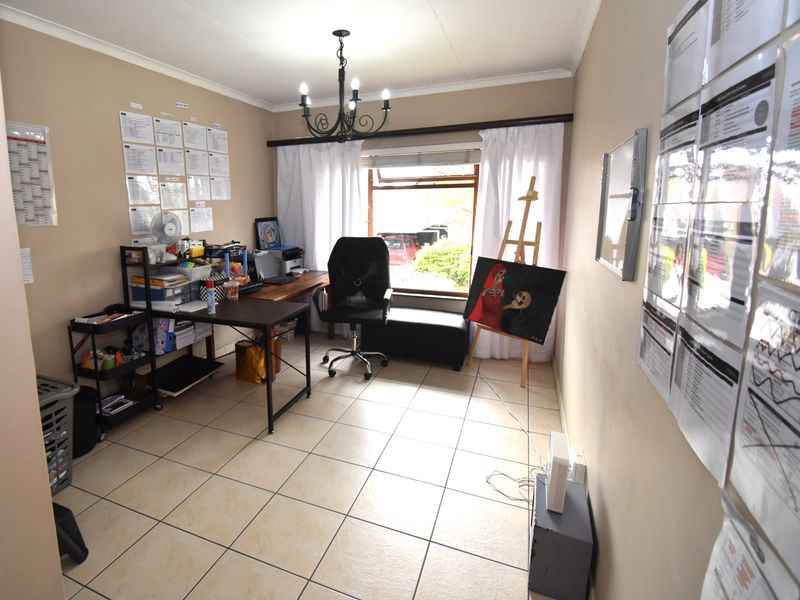 A functional home office space featuring tiled flooring, a central chandelier, and natural light from a window.