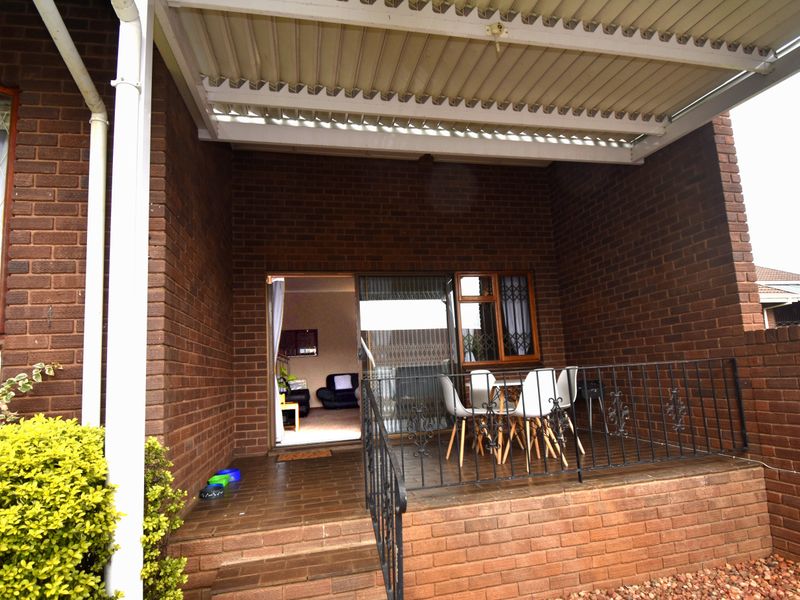 A covered brick patio featuring tiled flooring, a wrought iron railing, and direct access to the interior living space through a sliding glass door.