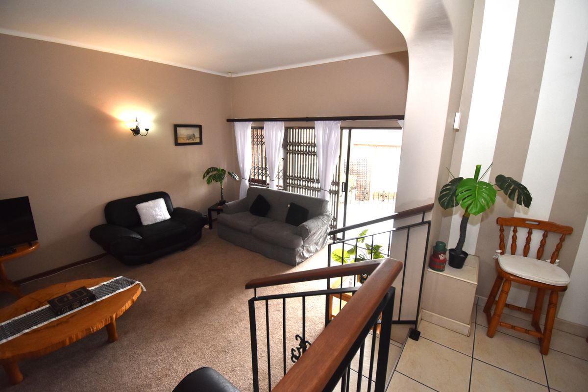 A living room area featuring carpeted flooring, wall-mounted lighting, and a sliding glass door with security gate leading to the exterior.