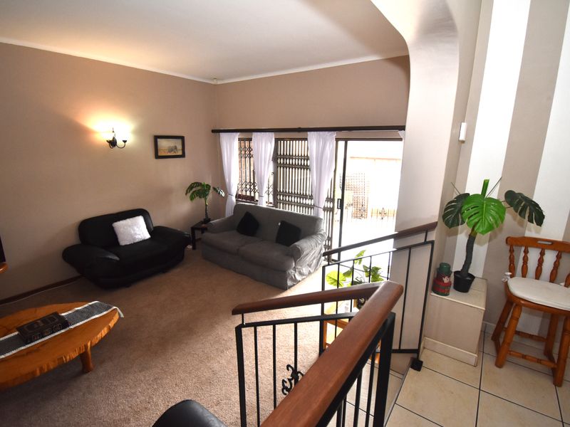 A living room area featuring carpeted flooring, wall-mounted lighting, and a sliding glass door with security gate leading to the exterior.