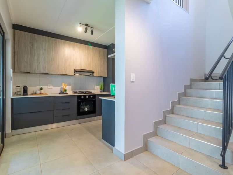 Modern kitchen featuring two-tone cabinetry, integrated appliances, and tiled flooring, adjacent to a staircase with a sleek metal handrail.