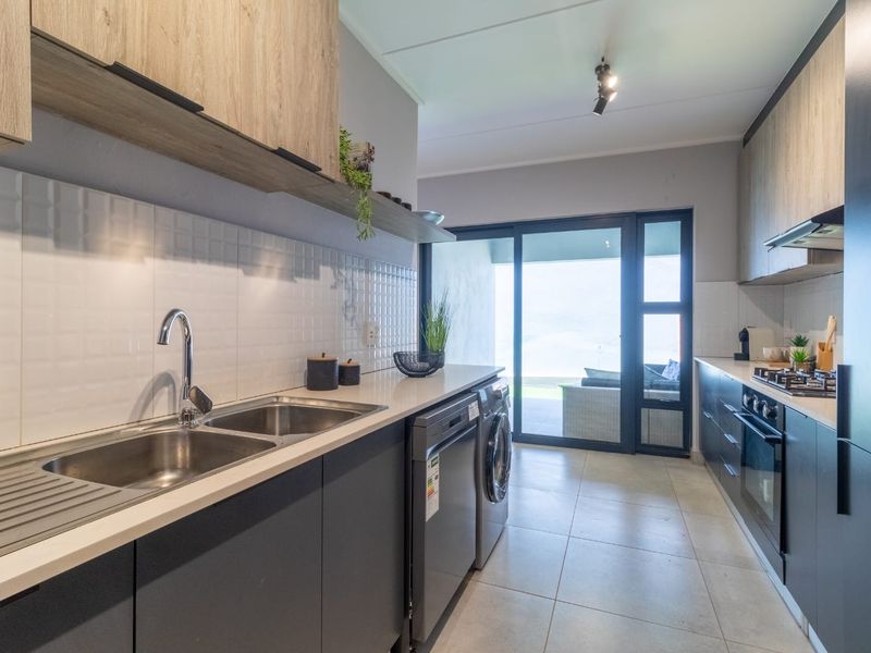 Modern galley-style kitchen featuring sleek dark cabinetry, light wood-look upper cabinets, gas hob, built-in oven, and direct access to an outdoor patio area.