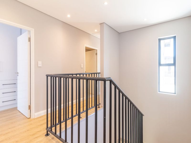 A bright, modern upstairs landing featuring laminate flooring, a sleek metal balustrade, and built-in storage cupboards.