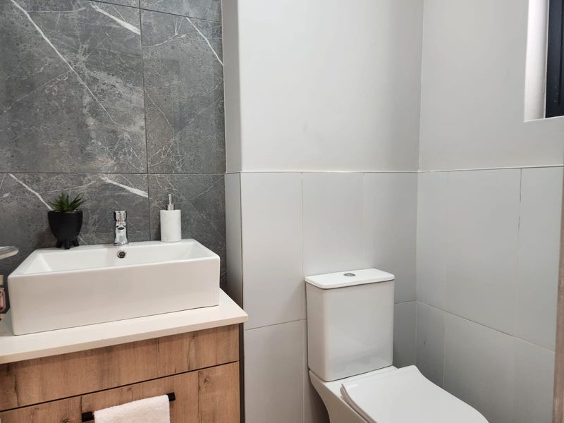 Modern bathroom featuring a wood-finish vanity with a vessel sink, marble-effect wall tiling, and a clean white toilet.