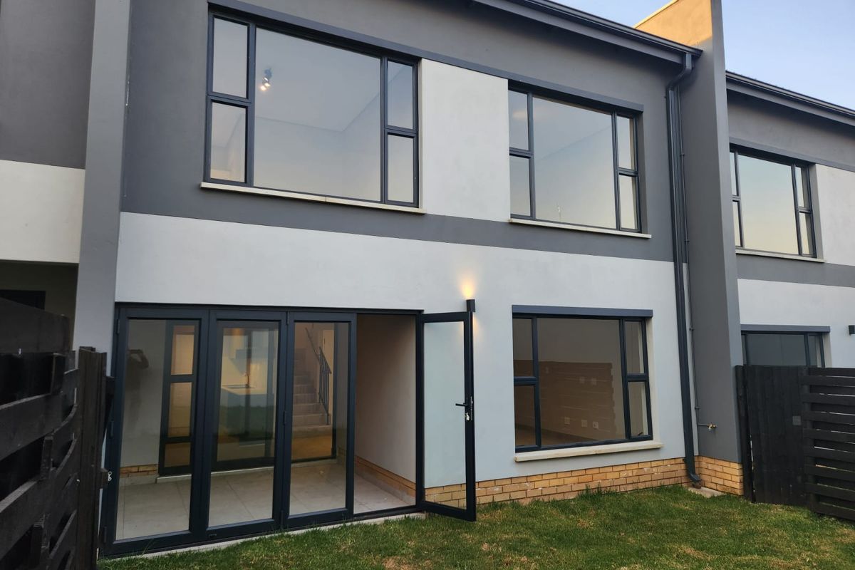 Rear elevation of a modern townhouse featuring contemporary grey and white facade, large aluminium windows, and folding glass doors leading to the garden.