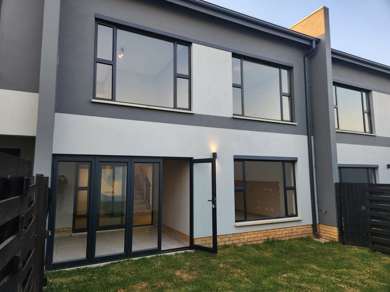 Rear elevation of a modern townhouse featuring contemporary grey and white facade, large aluminium windows, and folding glass doors leading to the garden.