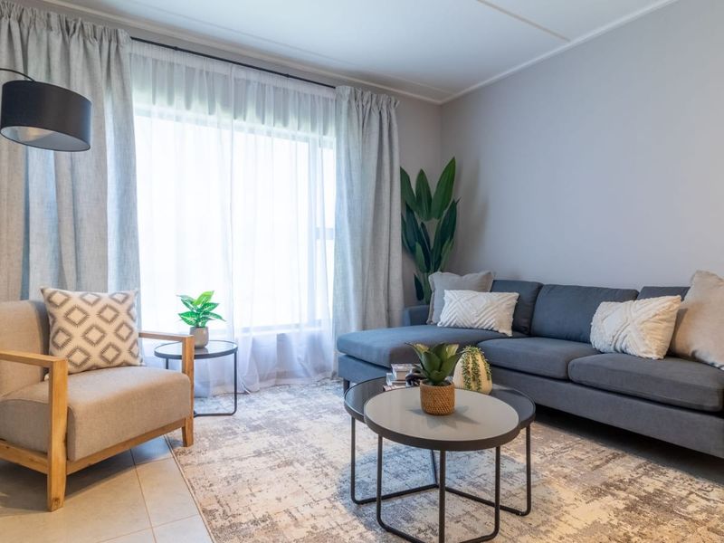 A bright and well-maintained living room featuring neutral tiled flooring and a large window with installed curtain tracks.