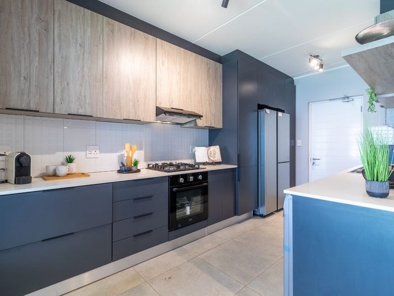 Modern kitchen featuring two-tone cabinetry, stone countertops, integrated gas hob, electric oven, and sleek tiled flooring in a contemporary townhouse setting.
