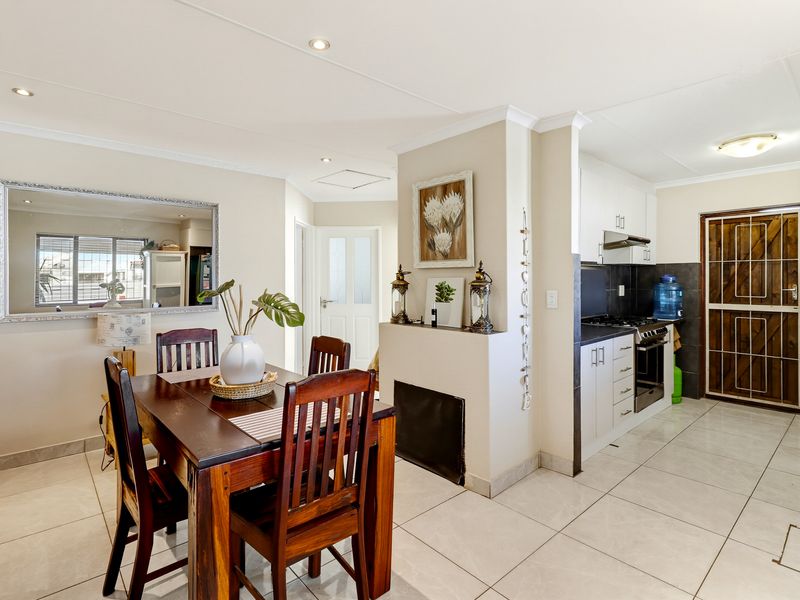 Open-plan dining area adjacent to a functional kitchen featuring white cabinetry, tiled floors, and modern recessed lighting.