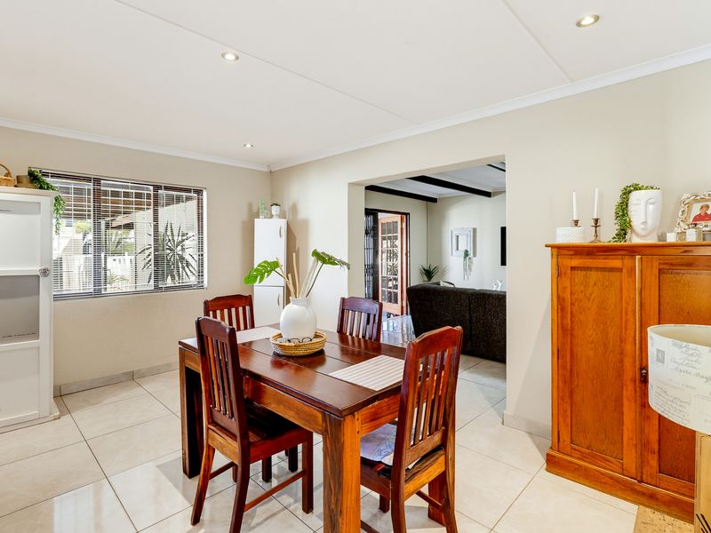 A bright dining room featuring neutral tiled flooring, recessed downlighting, and large windows with venetian blinds, offering a seamless flow into the adjacent living area.