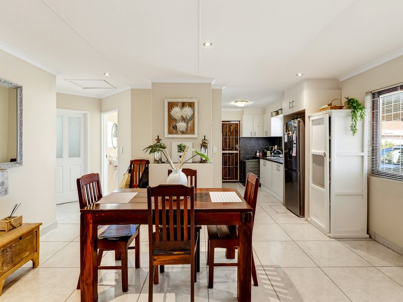 An open-plan dining and kitchen area featuring tiled flooring, recessed lighting, and functional kitchen cabinetry with a clean, neutral aesthetic.