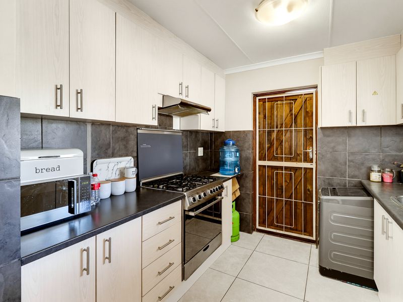 Functional kitchen featuring light wood-finish cabinetry, dark countertops, a gas stove with extractor fan, and direct access to the exterior via a security gate.
