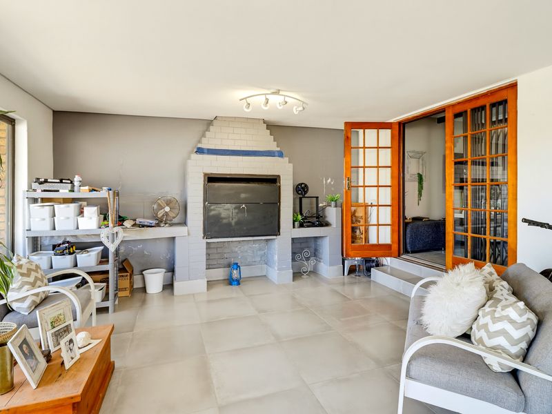 Covered patio area featuring a built-in braai, tiled flooring, and wooden french doors providing access to the interior living space.