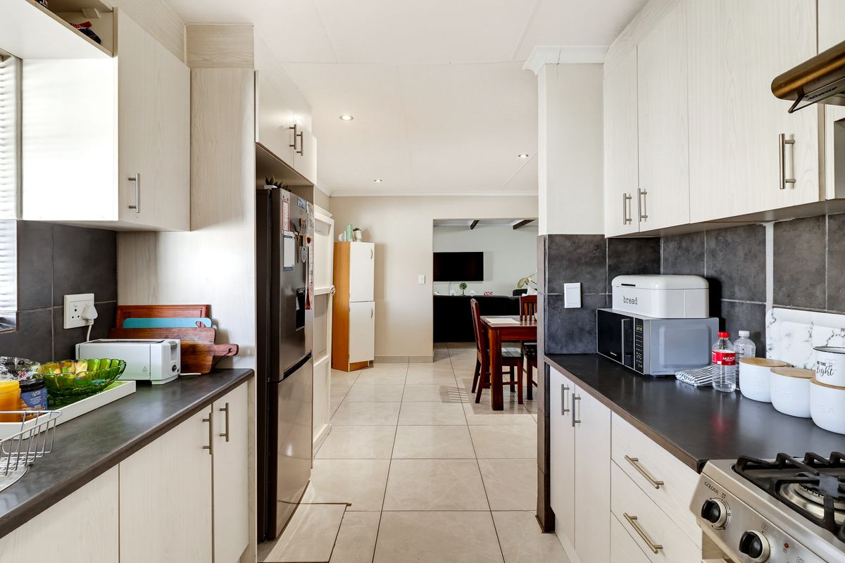 A functional kitchen featuring light-toned cabinetry, dark countertops, a gas hob with extractor, and tiled flooring, leading into an open-plan dining and living area.