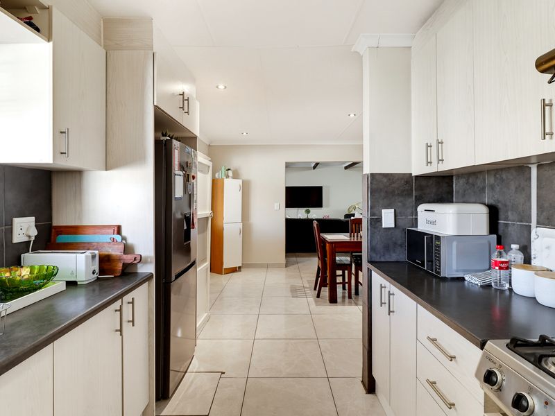 A functional kitchen featuring light-toned cabinetry, dark countertops, a gas hob with extractor, and tiled flooring, leading into an open-plan dining and living area.