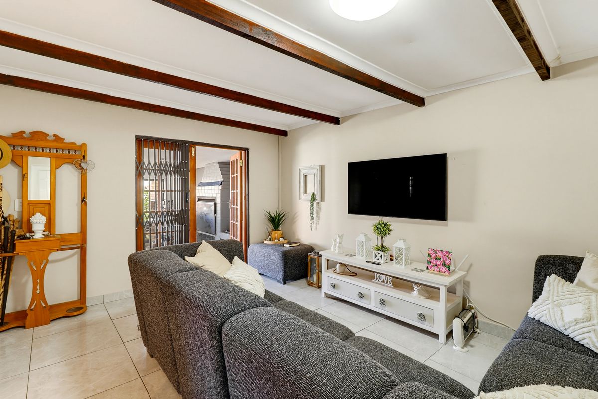 A comfortable living room featuring exposed timber ceiling beams, tiled flooring, and a sliding door providing access to an outdoor area.