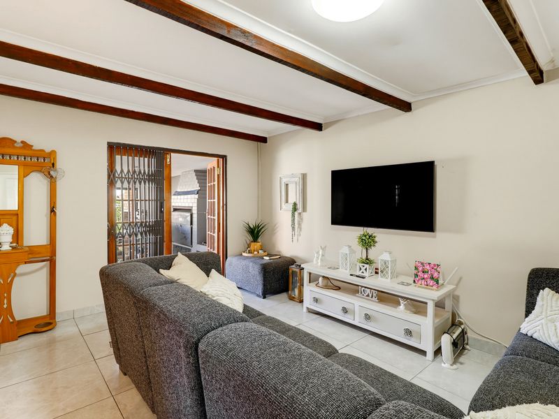 A comfortable living room featuring exposed timber ceiling beams, tiled flooring, and a sliding door providing access to an outdoor area.