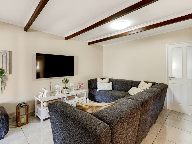 A comfortable living room featuring exposed timber ceiling beams, neutral wall finishes, and tiled flooring, creating a warm and inviting atmosphere.