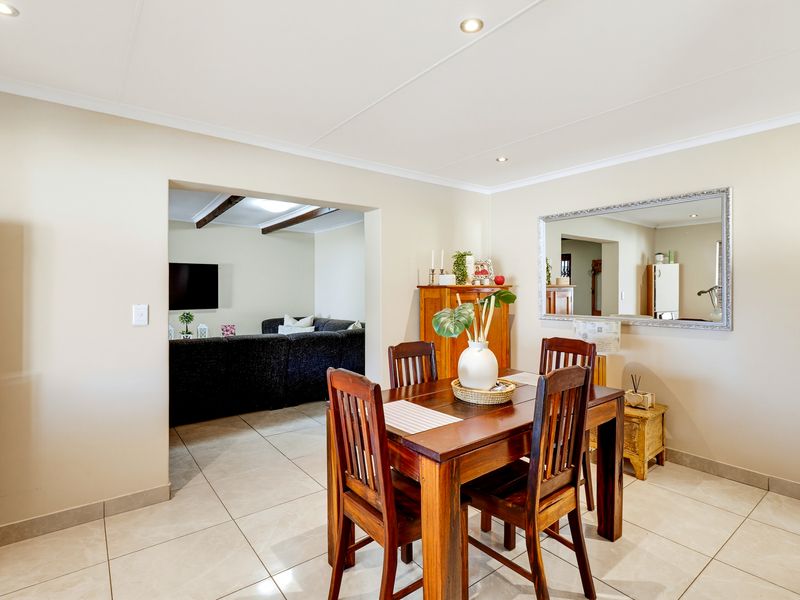 A bright dining room featuring neutral walls, tiled flooring, and recessed lighting, with an open-plan flow into the adjacent living area.