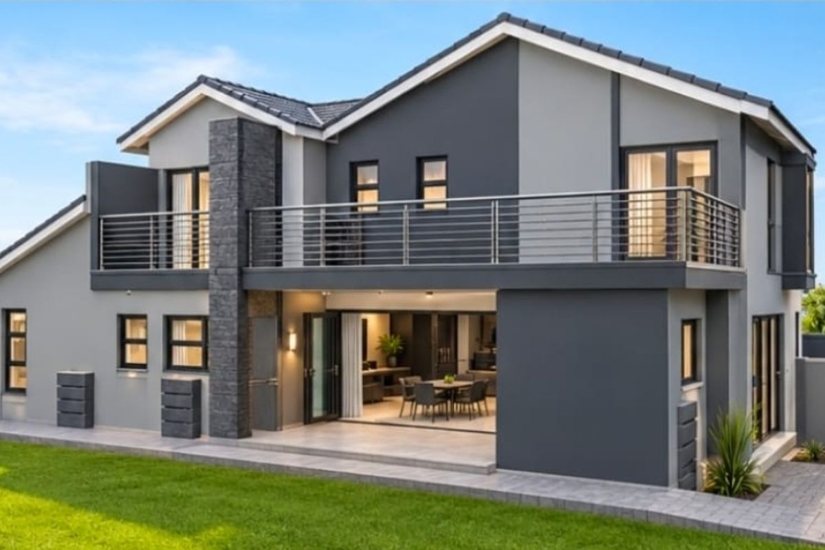 Modern double-story rear elevation featuring a spacious balcony, stone-clad architectural detail, large sliding doors opening to a paved patio, and a well-maintained garden.