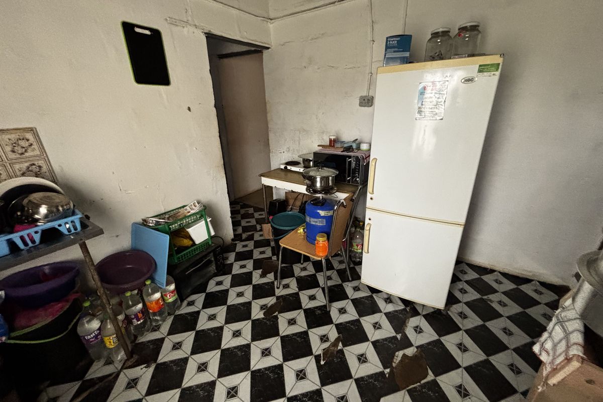 A basic kitchen area featuring checkered floor tiles, requiring significant renovation and repair to the wall finishes and flooring.