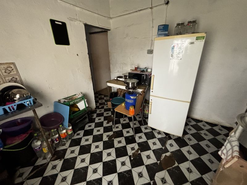 A basic kitchen area featuring checkered floor tiles, requiring significant renovation and repair to the wall finishes and flooring.