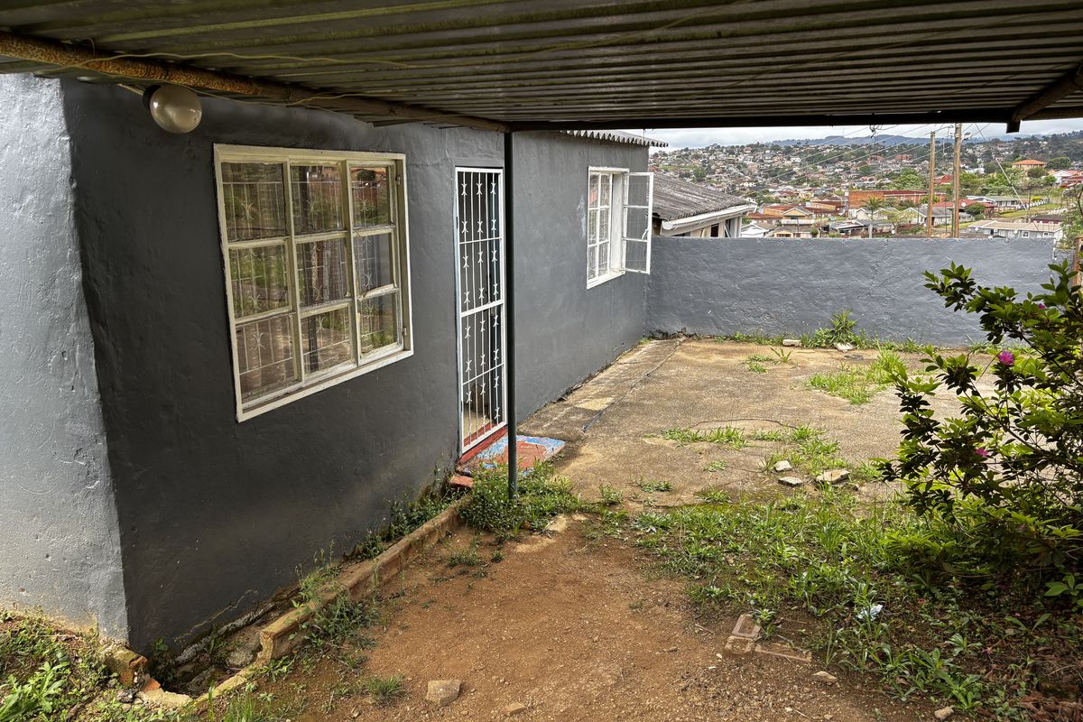 Rear exterior view of the townhouse featuring a covered patio area, security gate, and concrete paving with views of the surrounding neighborhood.