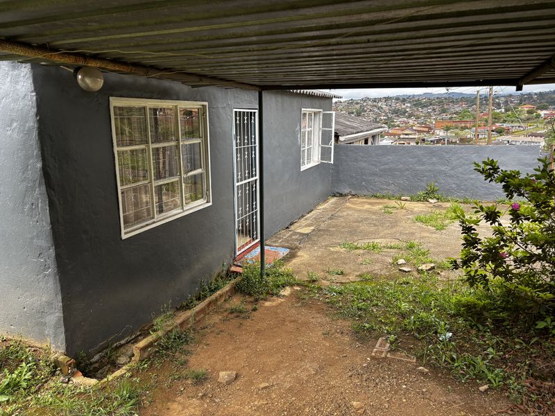 Rear exterior view of the townhouse featuring a covered patio area, security gate, and concrete paving with views of the surrounding neighborhood.