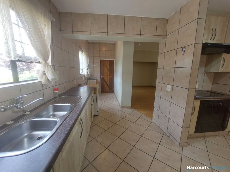 A functional kitchen featuring tiled walls and floors, double stainless steel sink, built-in cabinetry, and integrated oven with extractor fan.