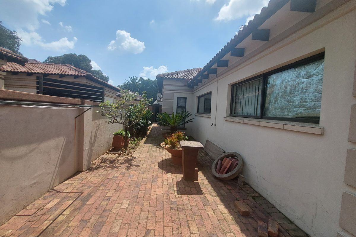 A side walkway featuring brick paving, tiled roofing with exposed rafters, and aluminium window frames along the exterior wall.