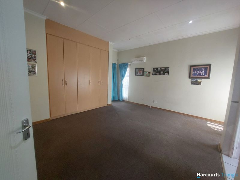 A spacious bedroom featuring built-in cupboards, carpeted flooring, and a wall-mounted split-system air conditioner.