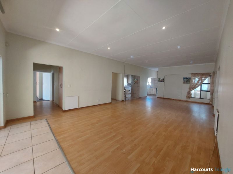 Spacious open-plan living area featuring a combination of laminate and tiled flooring, recessed downlighting, and neutral wall finishes.