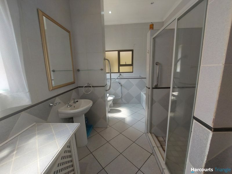 A functional bathroom featuring a pedestal basin, shower enclosure, bathtub, and toilet, finished with neutral wall and floor tiling.