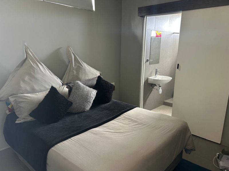 A bedroom featuring a sliding door leading to an en-suite bathroom with a wall-mounted basin and tiled finishes.