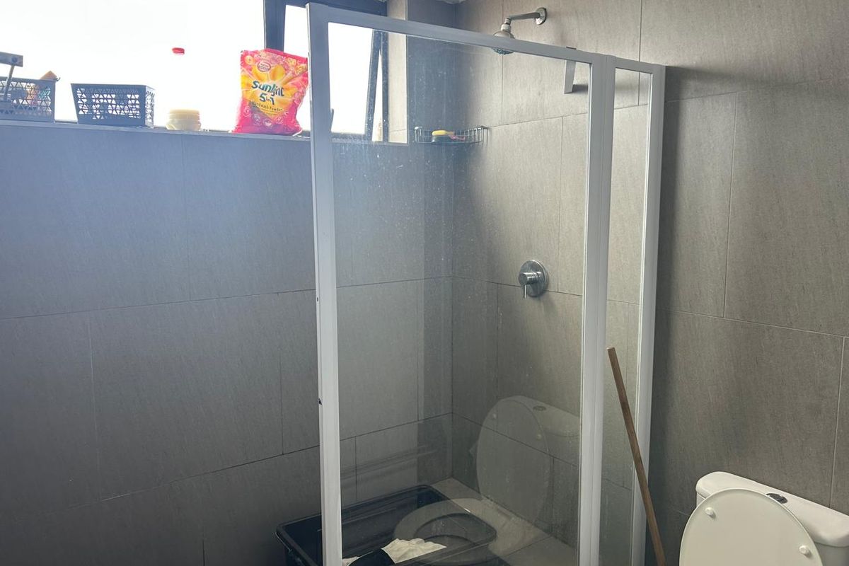 A functional bathroom featuring a glass-enclosed shower, wall-mounted shower head, and a standard toilet with grey wall tiling.